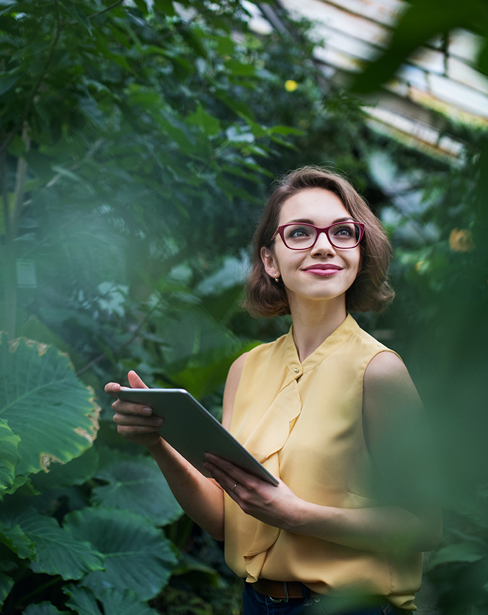Ung kvinna med glasögon och ipad bland växter